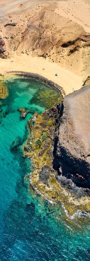 Luftfoto af Papagayo-stranden på Lanzarote, med gyldent sand, vulkanske klipper og turkis hav.